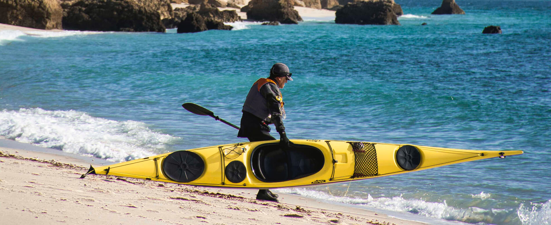 Man carrying yellow sit-in kayak heading to ocean