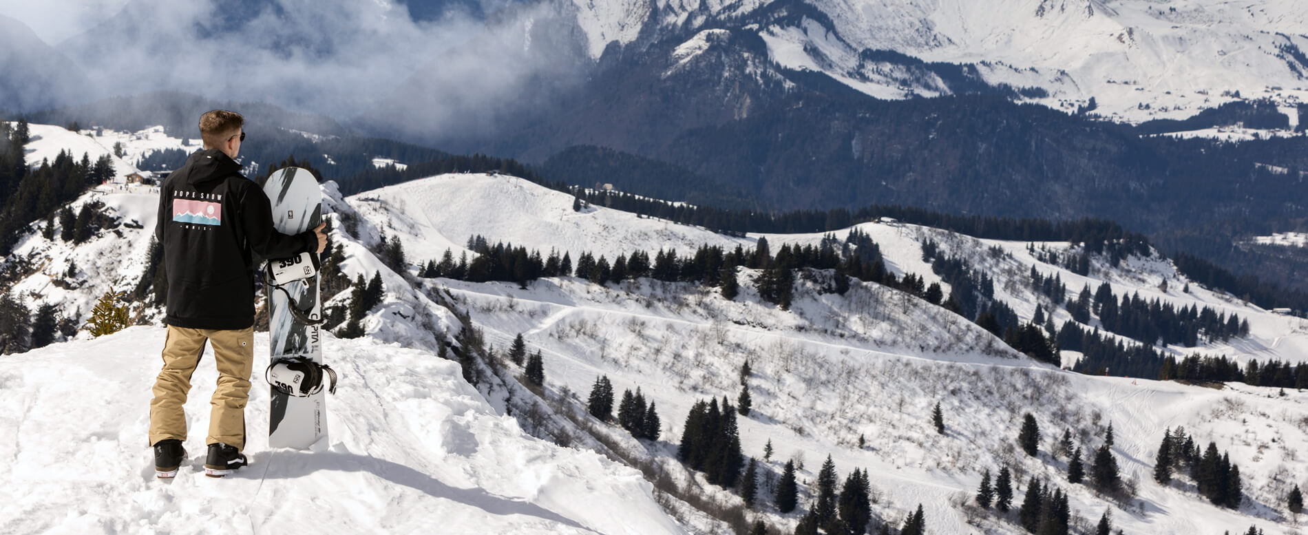 Man on the top of the snow cap mountain holding a snowboard